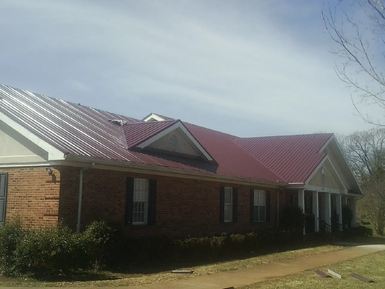Red metal roof with gabled entries on a long brick building, from a Hail Damage Roof Repair job in Hamburg