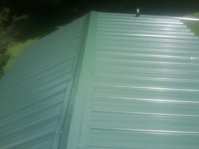 New green metal panels meeting at the ridge of a roof — Flat Roof Repair work by our crew in Hamburg