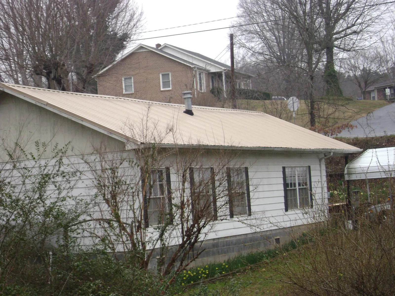 Tan metal roof on a white sided house set into a hillside — Commercial Roofing by Roofing Brothers in Hamburg